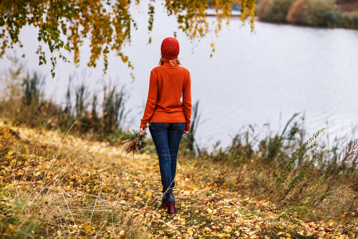 Rear view of person standing on riverbank in autumn holding bunch of dried flowers