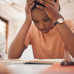 Young girl with hands on her head reading a book stressed